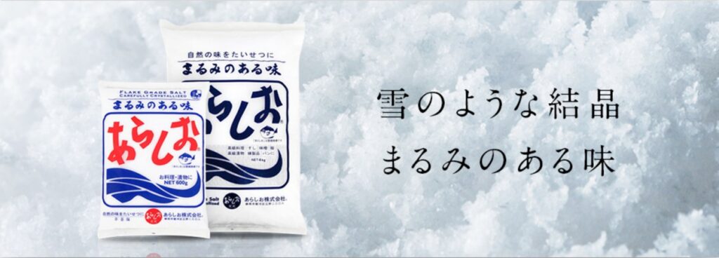 雪のような結晶を背景に、赤い文字と青い波を描いたあらしおの袋が2つ並び、「雪のような結晶 まるみのある味」と書かれている